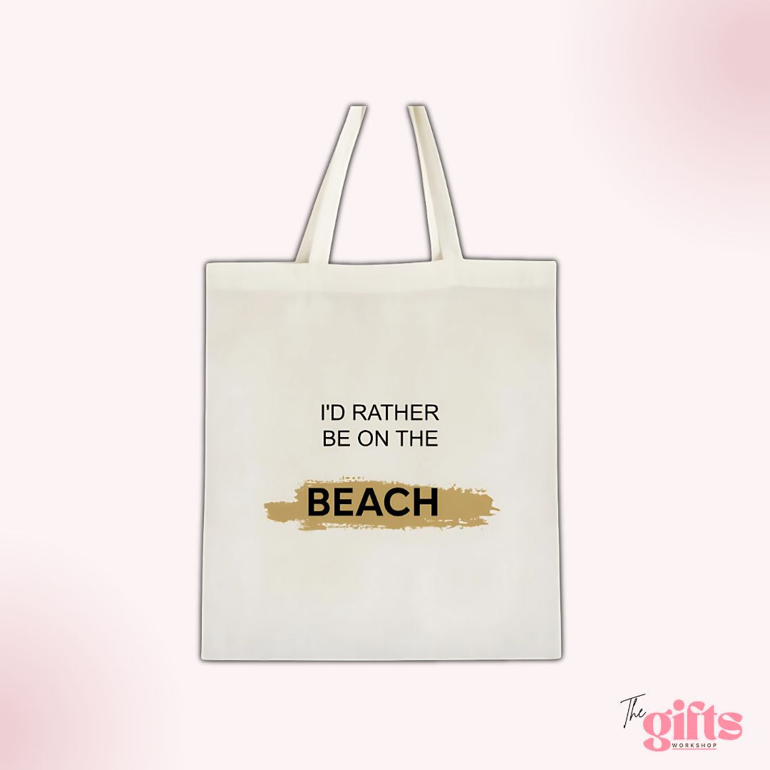 White tote bag with 'I'D RATHER BE ON THE BEACH' text and gold brushstroke background, from The Gifts Workshop