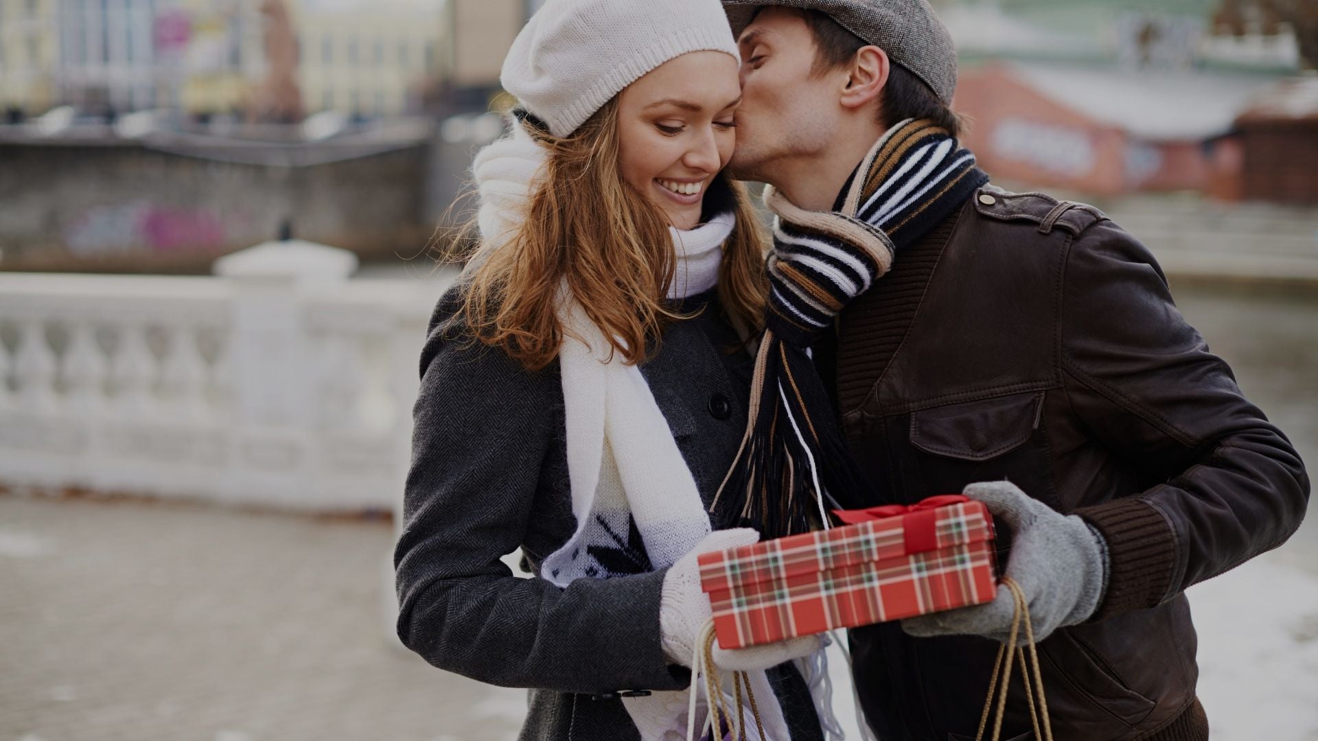 A man and woman share a kiss while holding a beautifully wrapped gift, capturing a moment of love and celebration