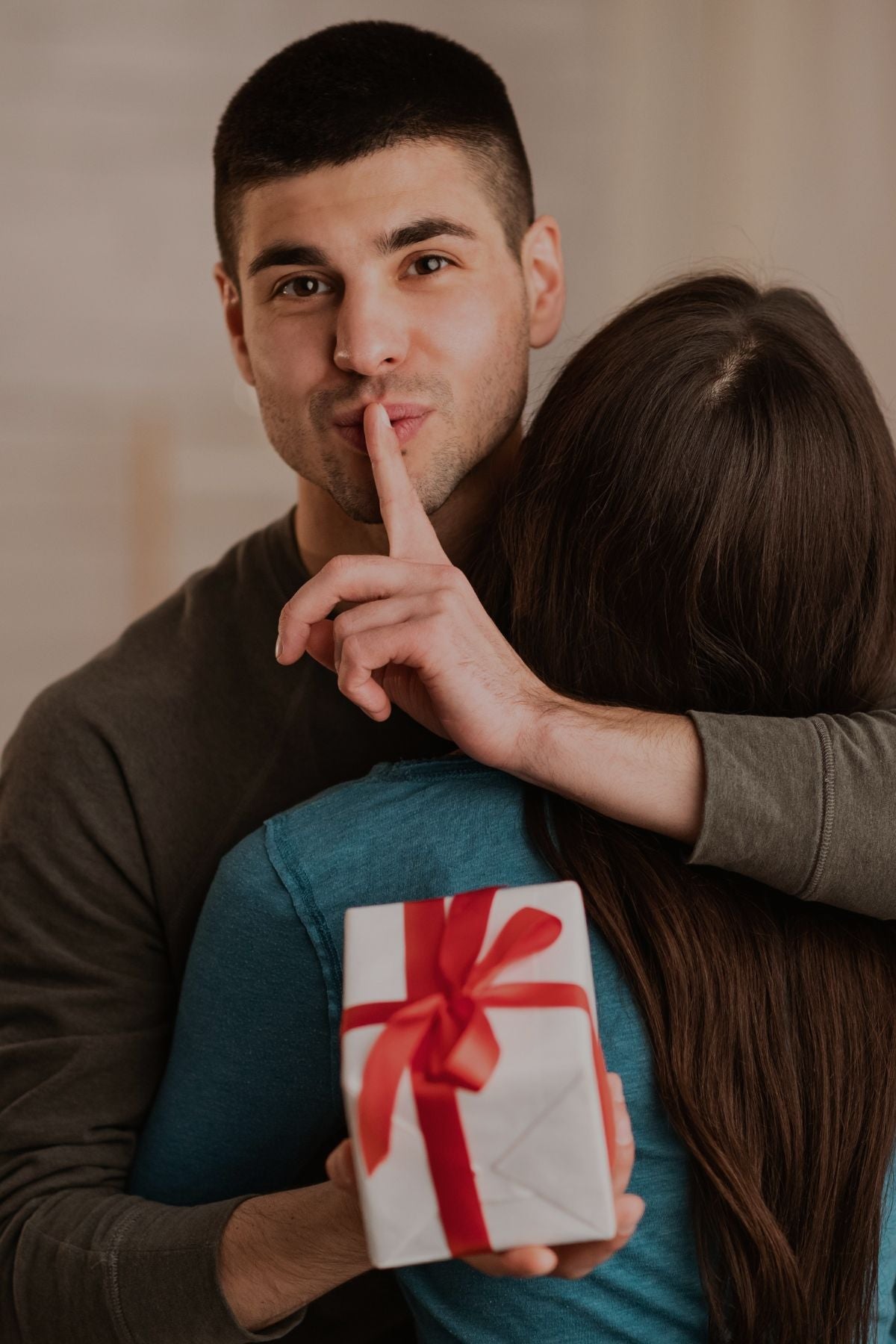 Man presents a gift to a woman, who playfully gestures with her finger on her lips, suggesting a secret or surprise